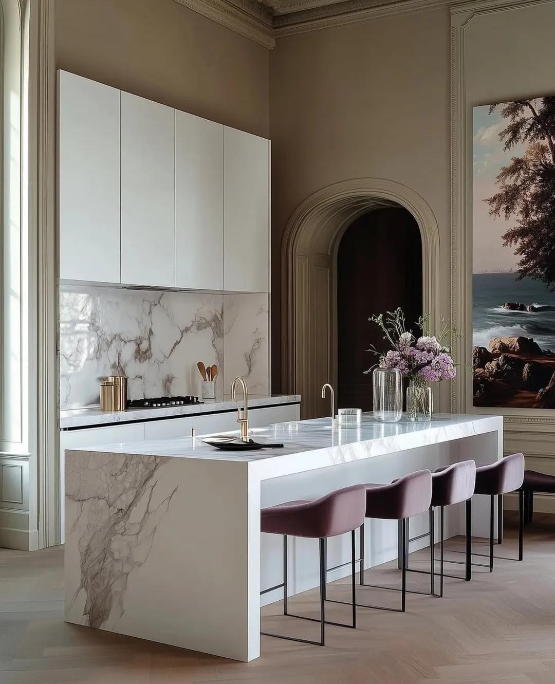 Cocina moderna con muebles blancos y una isla de mármol, decorada con flores y arte.