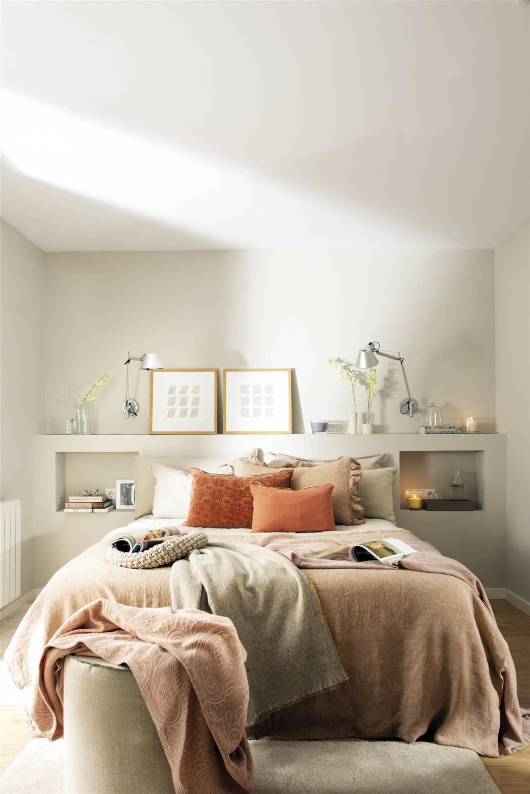 Dormitorio moderno con cama grande, cojines en tonos cálidos y decoración minimalista.