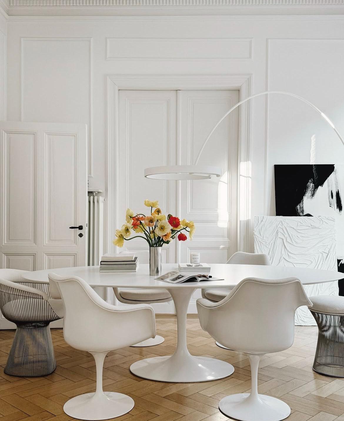 Comedor moderno con mesa blanca, sillas elegantes y flores coloridas en el centro.